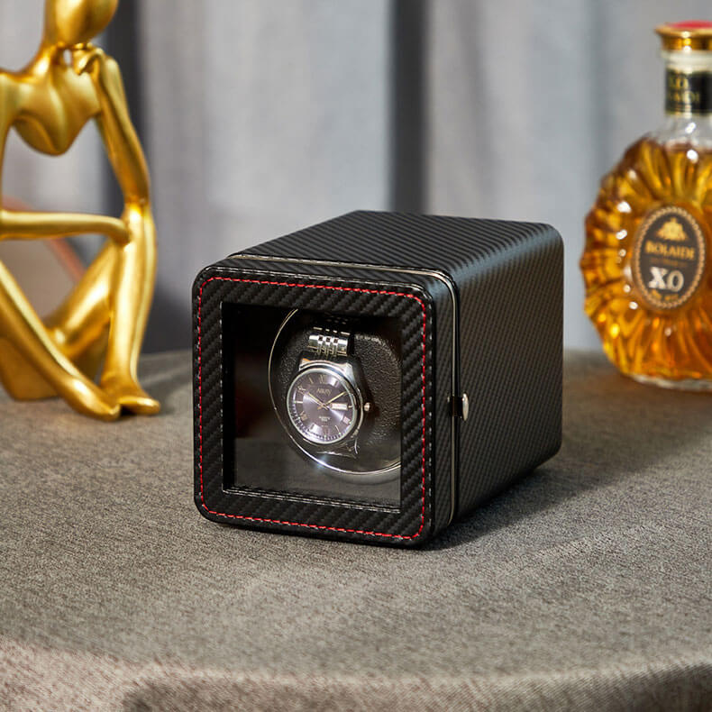 Una caja enrolladora de reloj automática individual con un exterior con textura de fibra de carbono negra con costuras en contraste rojas y una ventana de visualización de vidrio transparente.