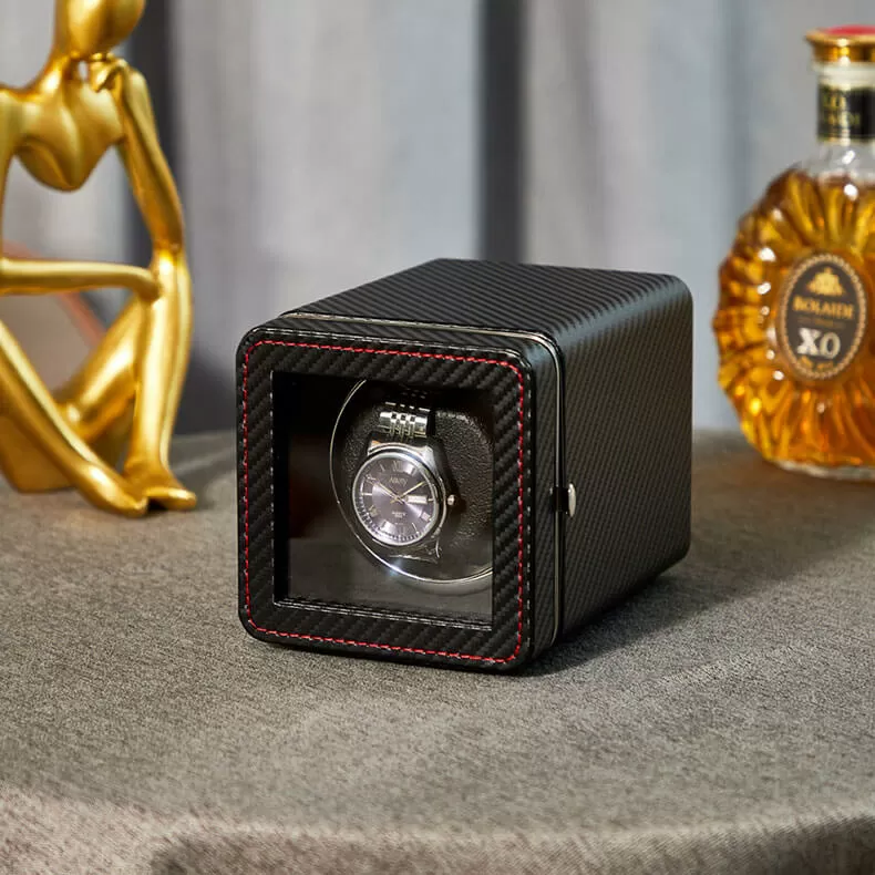 A single automatic watch winder box featuring a black carbon fiber textured exterior with red contrast stitching and a clear glass viewing window